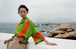 Model in a green and orange jacket on coastal rocks, ELLE Hong Kong editorial by Filip Freytag 